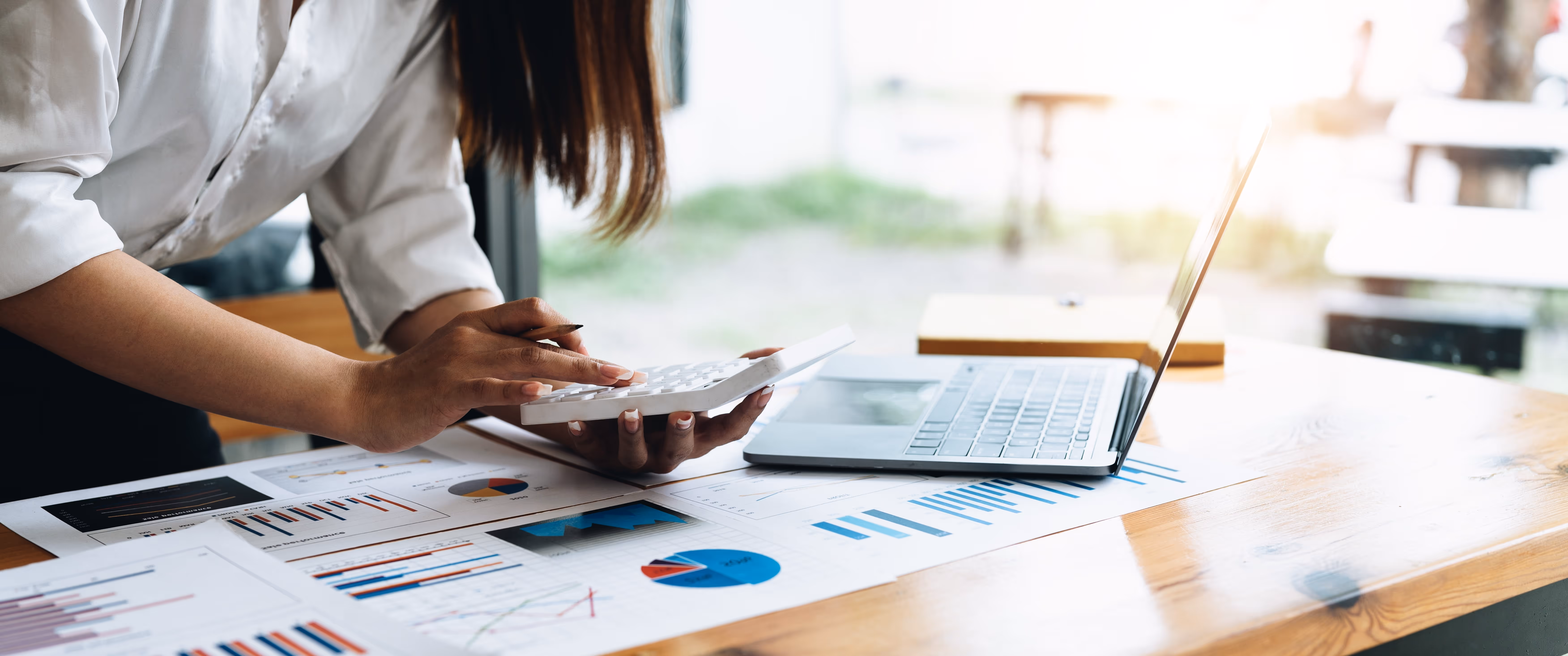 A woman holding a calculator works with her many sheet spread on her desk