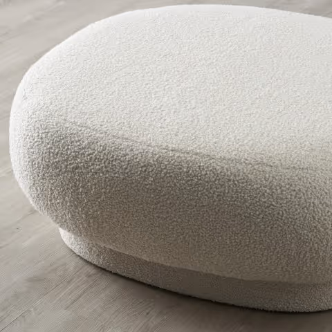 Pouf rond blanc crème en tissu bouclé sur un sol en bois clair.