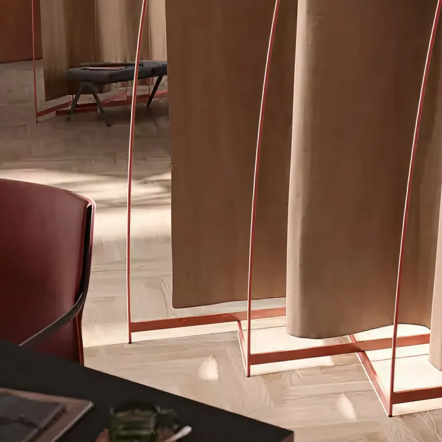 Modern room divider with beige fabric panels suspended in copper-colored metal frames on a light wood floor.