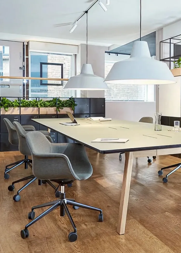 Modern conference room with a large table, gray swivel chairs on wheels, hanging white lamps, and wooden flooring.