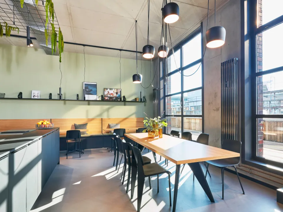 Modern dining area with a wooden table, black chairs, large windows letting in natural light, and hanging pendant lights.