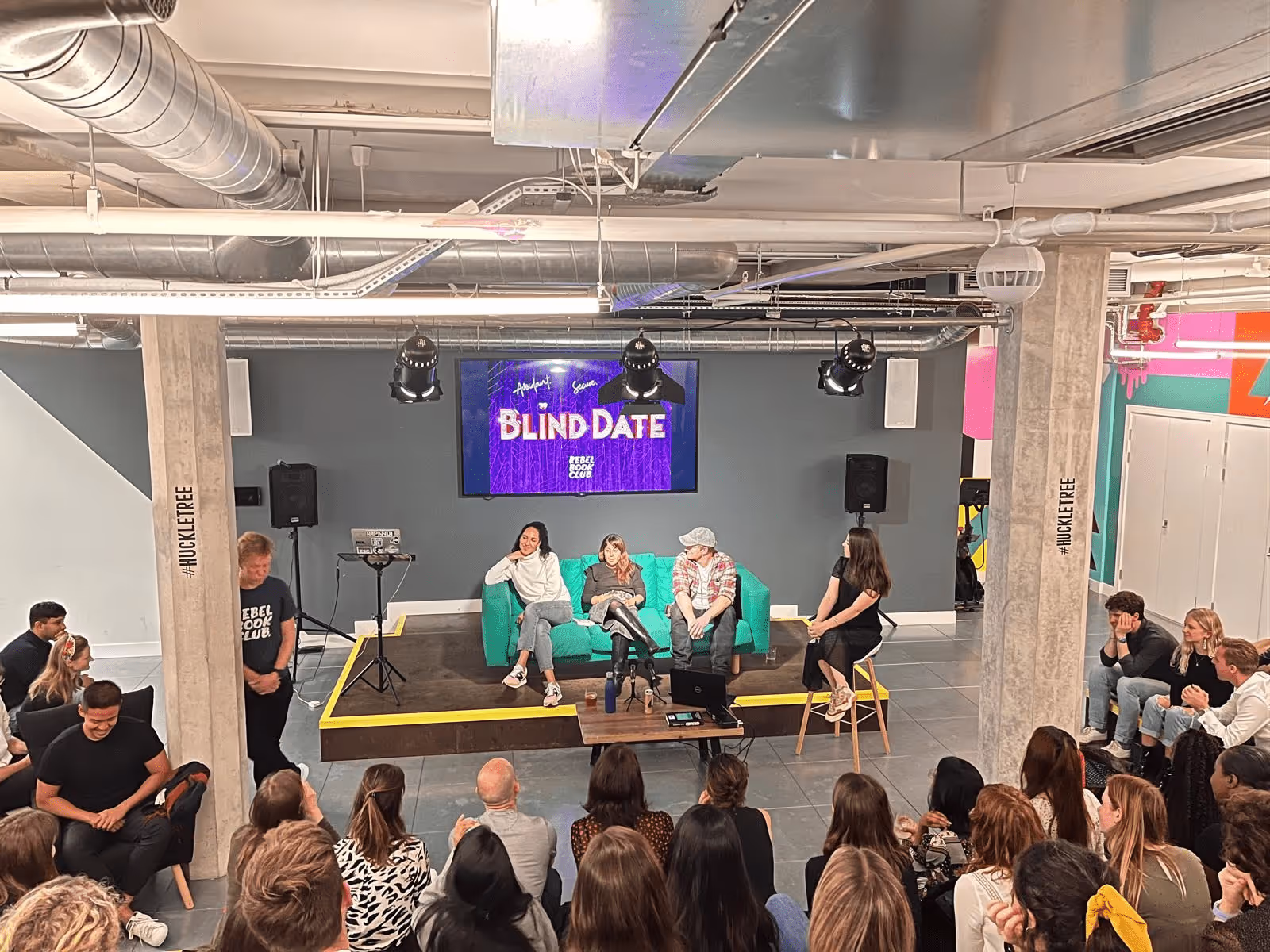 Club members sat on sofa on a stage in front of Blind Date logo