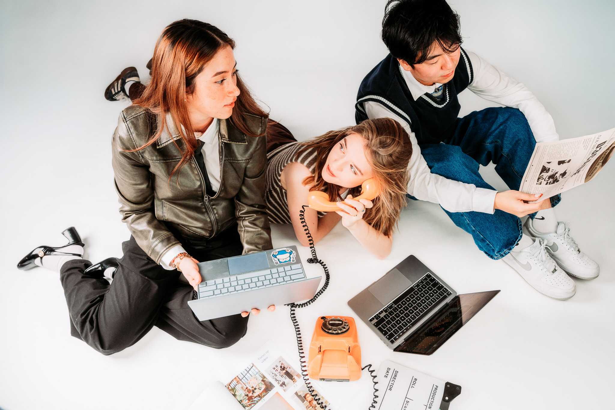 Three young people sitting on the floor with laptops, a rotary phone, and documents.