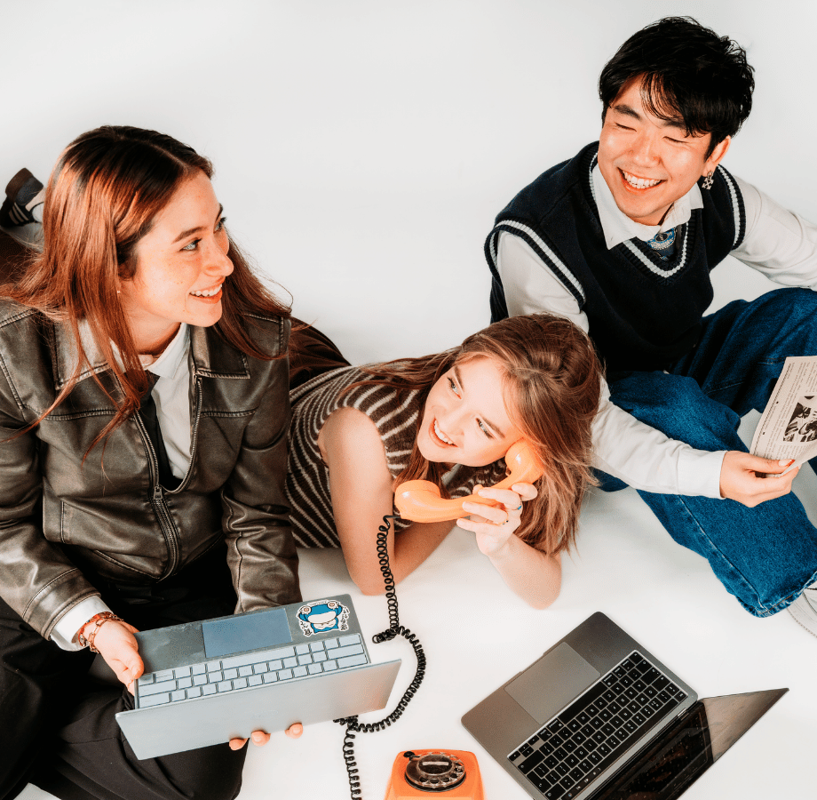 Three young people sitting on the floor with laptops, a rotary phone, and documents.
