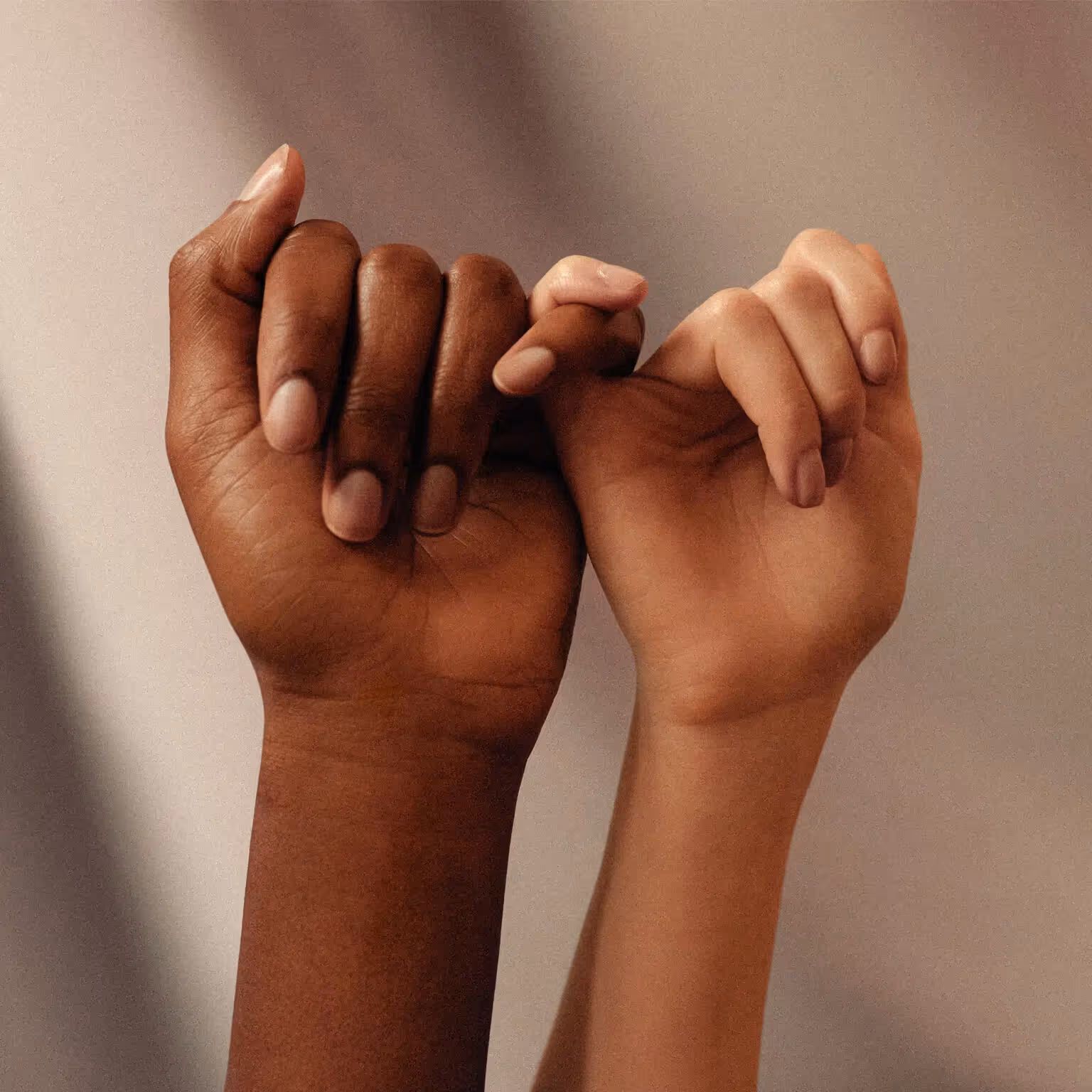 Close-up of two hands, one dark-skinned and one light-skinned, linking pinky fingers together.