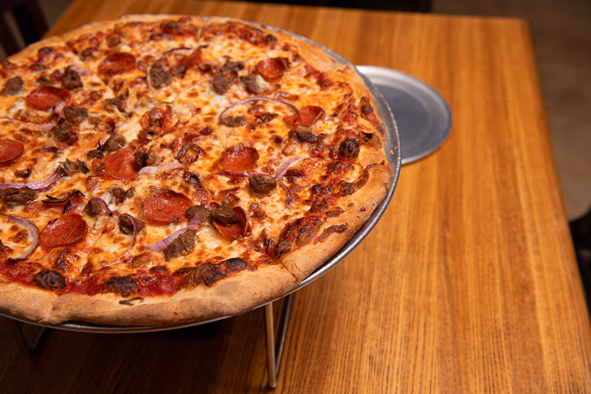 Pepperoni pizza with sausage and red onion slices on a metal stand over a wooden table.