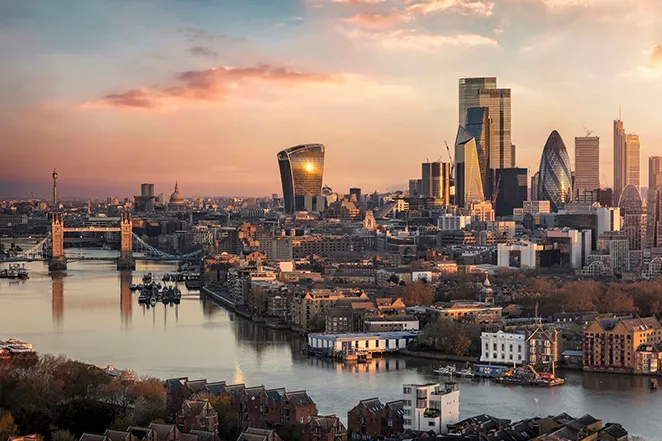 Exterior of a modern industrial building with a large sign reading 'drax' under a partly cloudy sky and digital light trails.