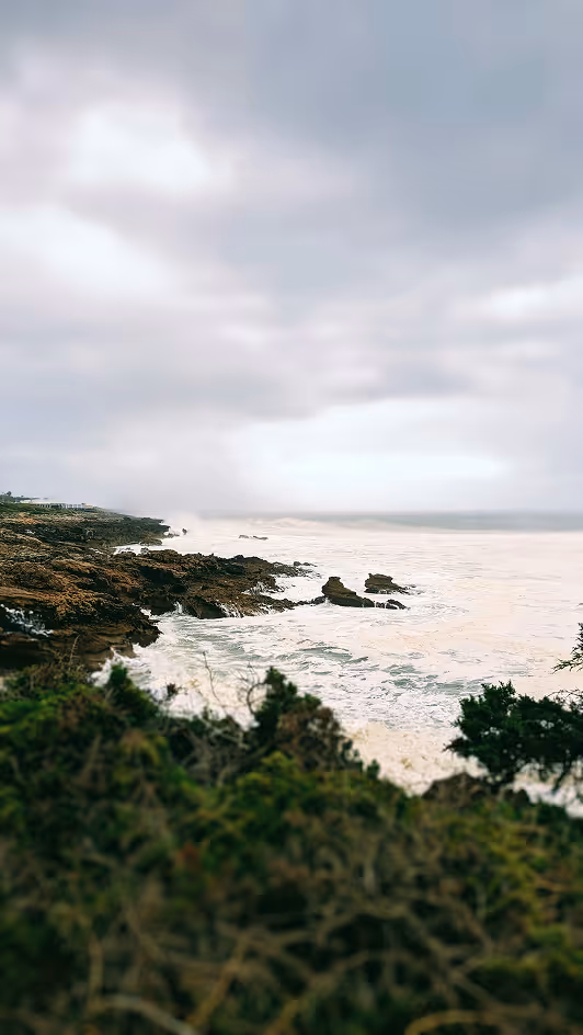 Rocky coastline with waves crashing and cloudy sky above during daytime.