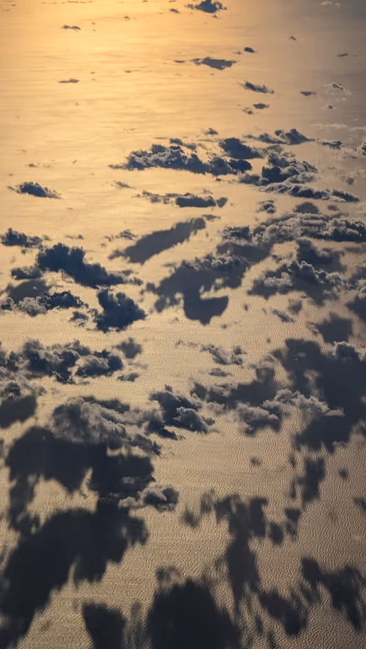 Cloud shadows cast on a shimmering ocean surface during golden hour.