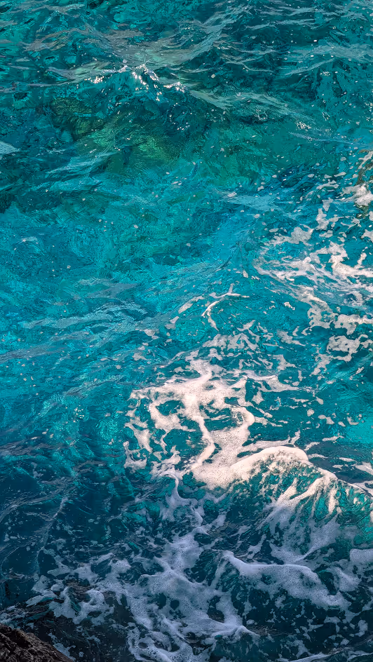 Clear turquoise ocean water with white foam and rocks visible beneath the surface.