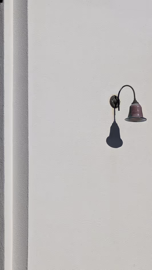 Single metal wall lamp casting a shadow on a smooth, light gray textured wall.