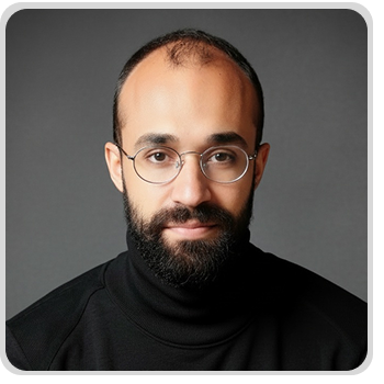 Portrait of a bearded man with glasses wearing a black turtleneck against a gray background. The man in image is Guto Cidreira.