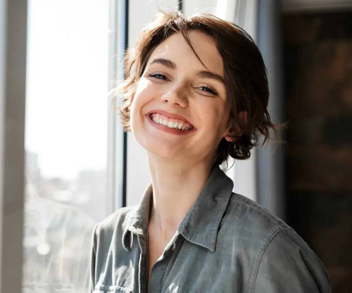 A woman smiling and looking out a window.