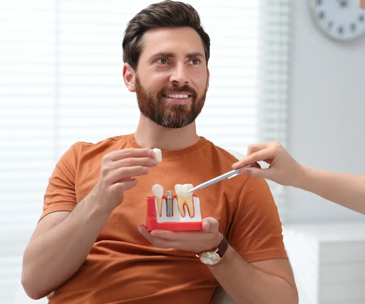A man holding a toothbrush and a model of a tooth.