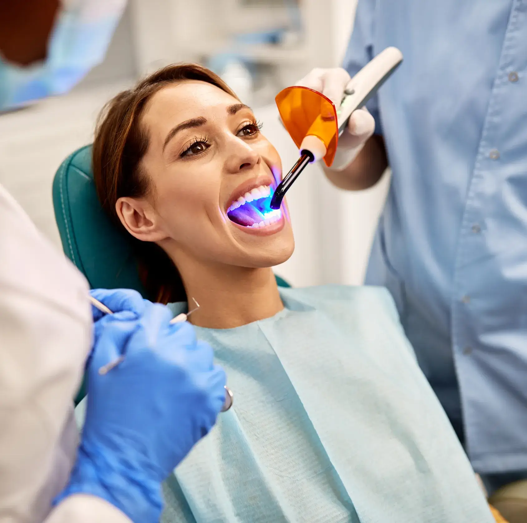 A woman sitting in a dentist chair with a toothbrush in her mouth.