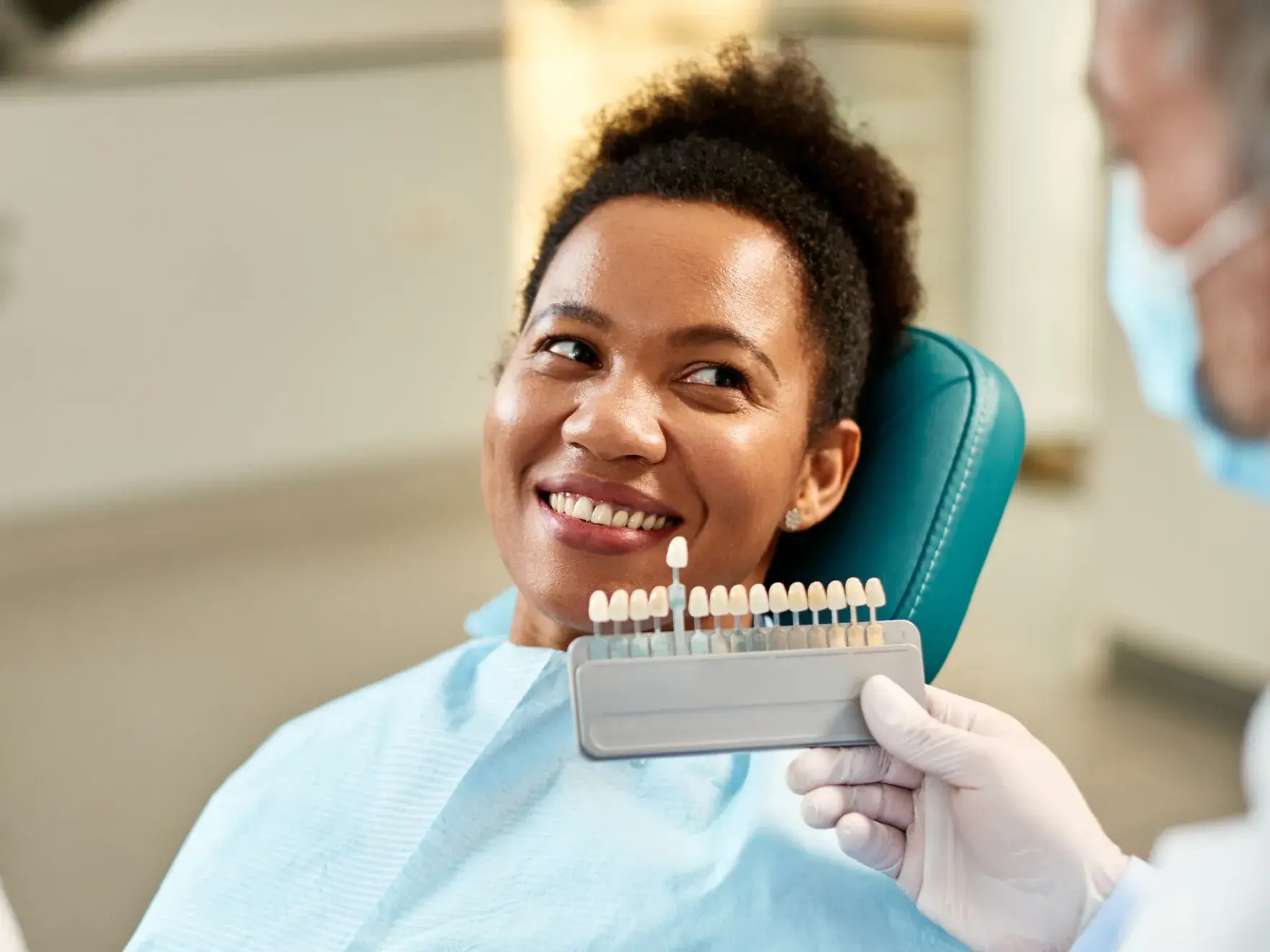 A smiling woman in a dentist chair holding a toothbrush.