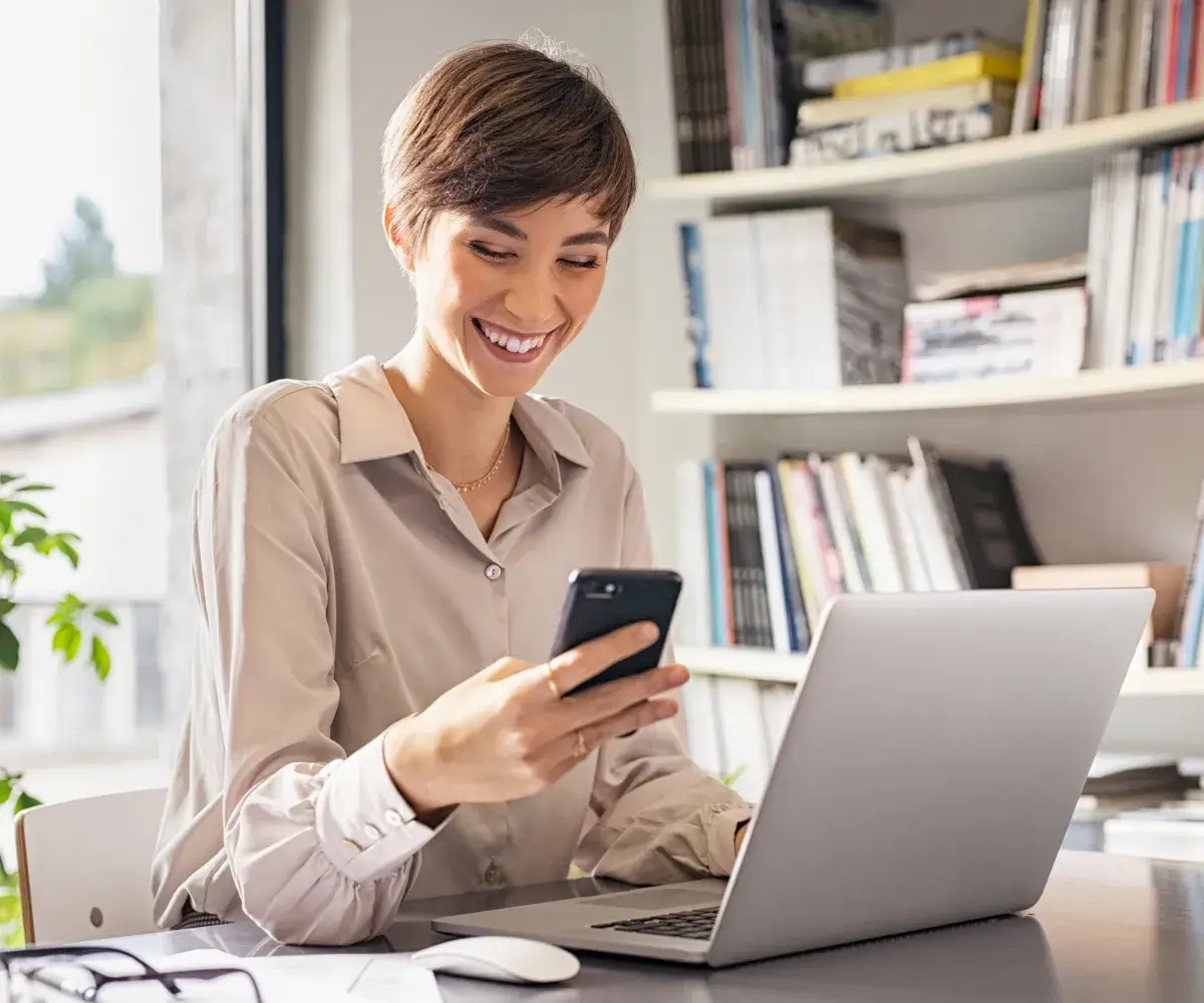 A woman sitting at a desk looking at a cell phone.
