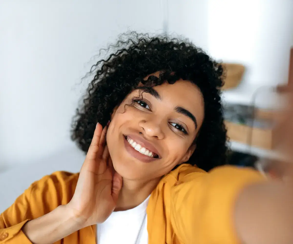 A woman smiles as she holds her hand up to her face.