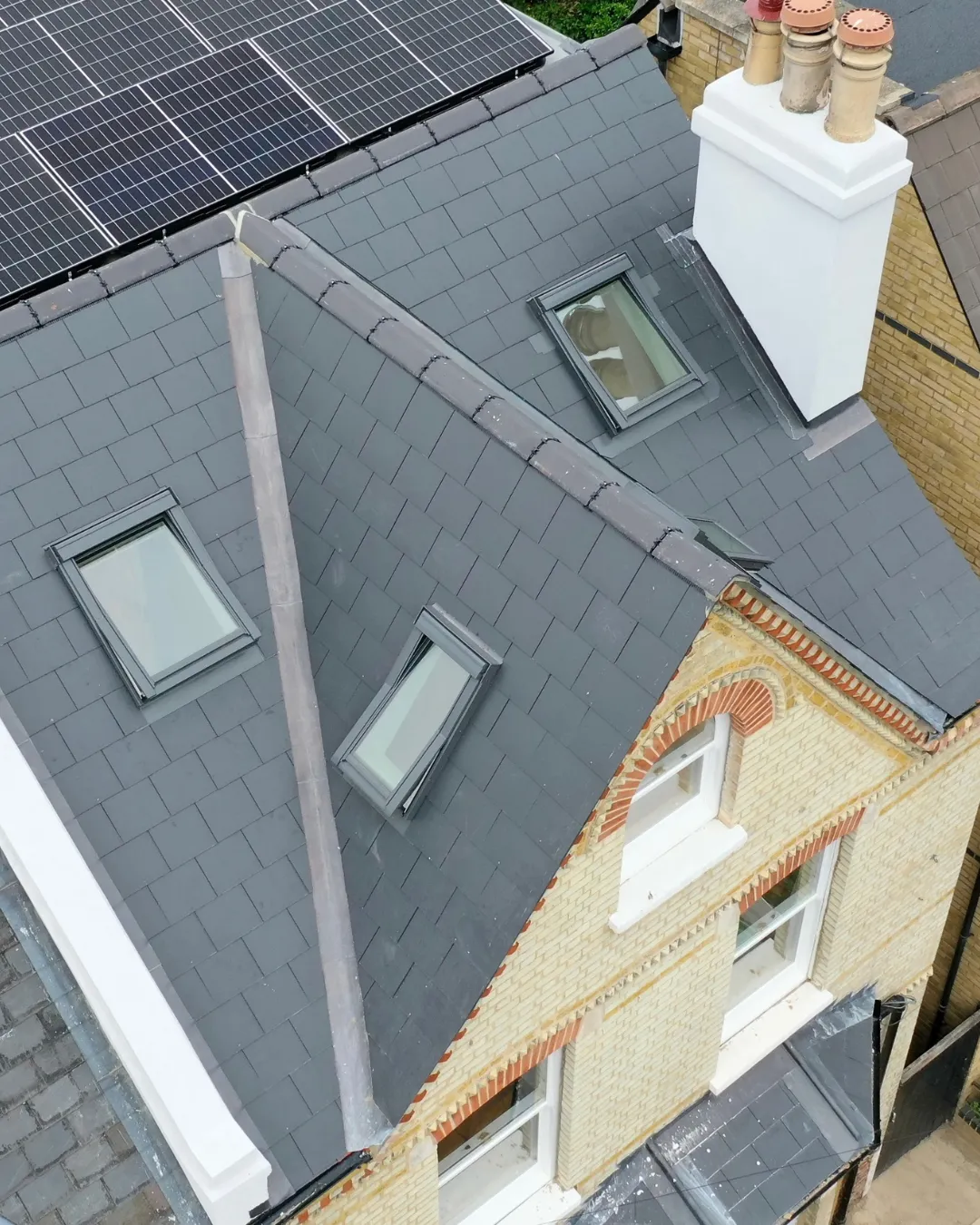 A finished slate roof with rooflights, solar panels and a rebuilt chimney stack