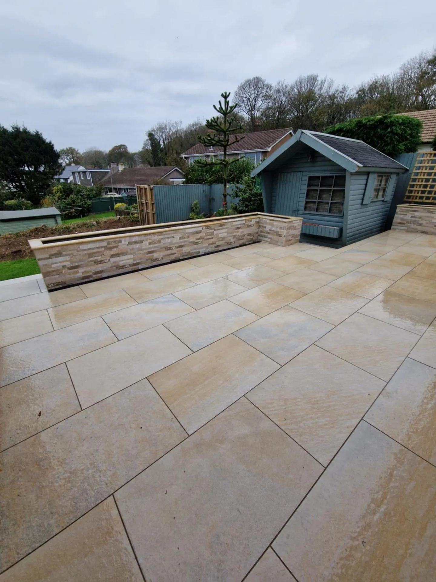 A sandstone patio with a rendered raised bed and garden room behind