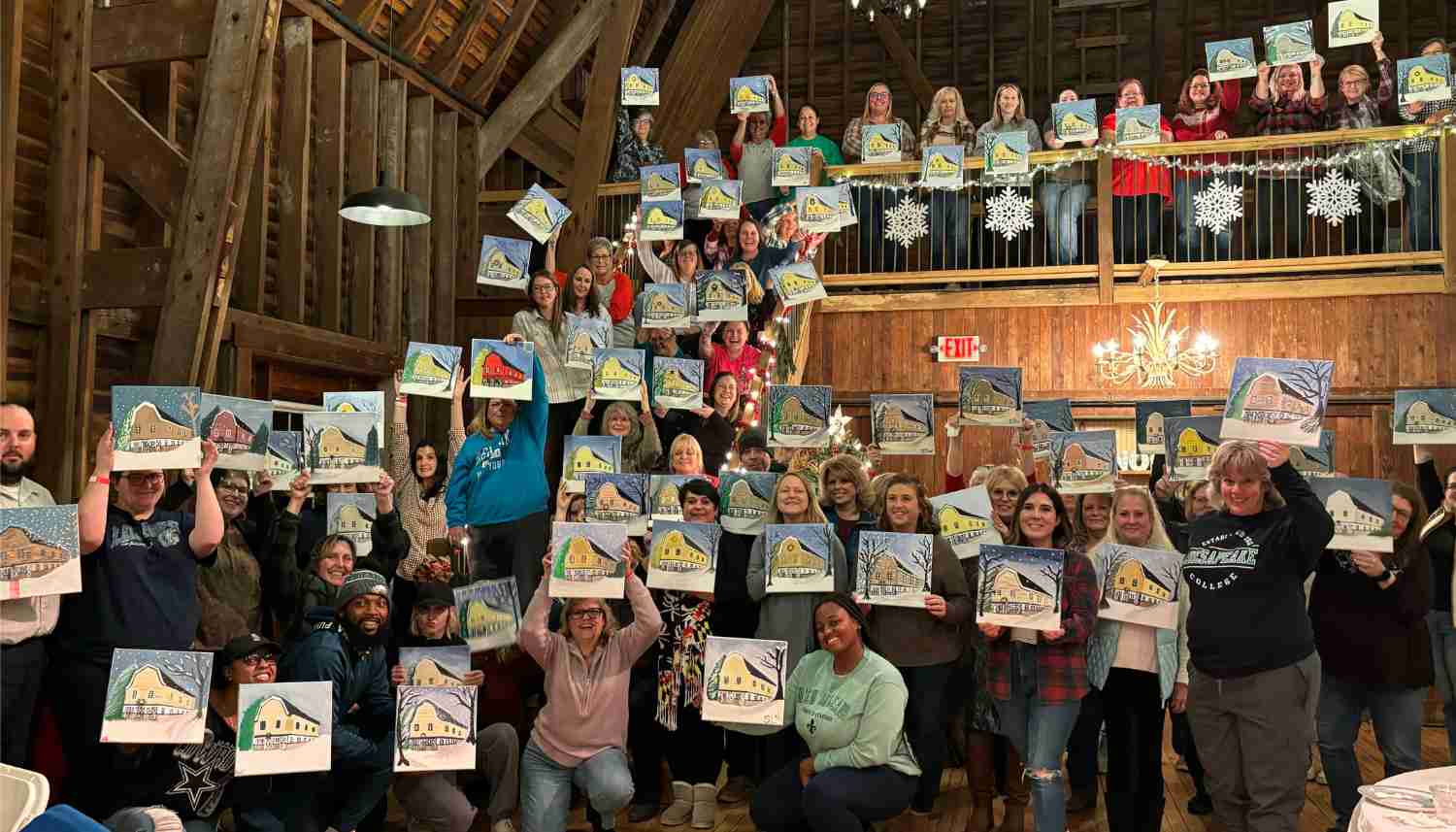Large group of people posing indoors, each holding a painting of a colorful cupcake on a bright background.