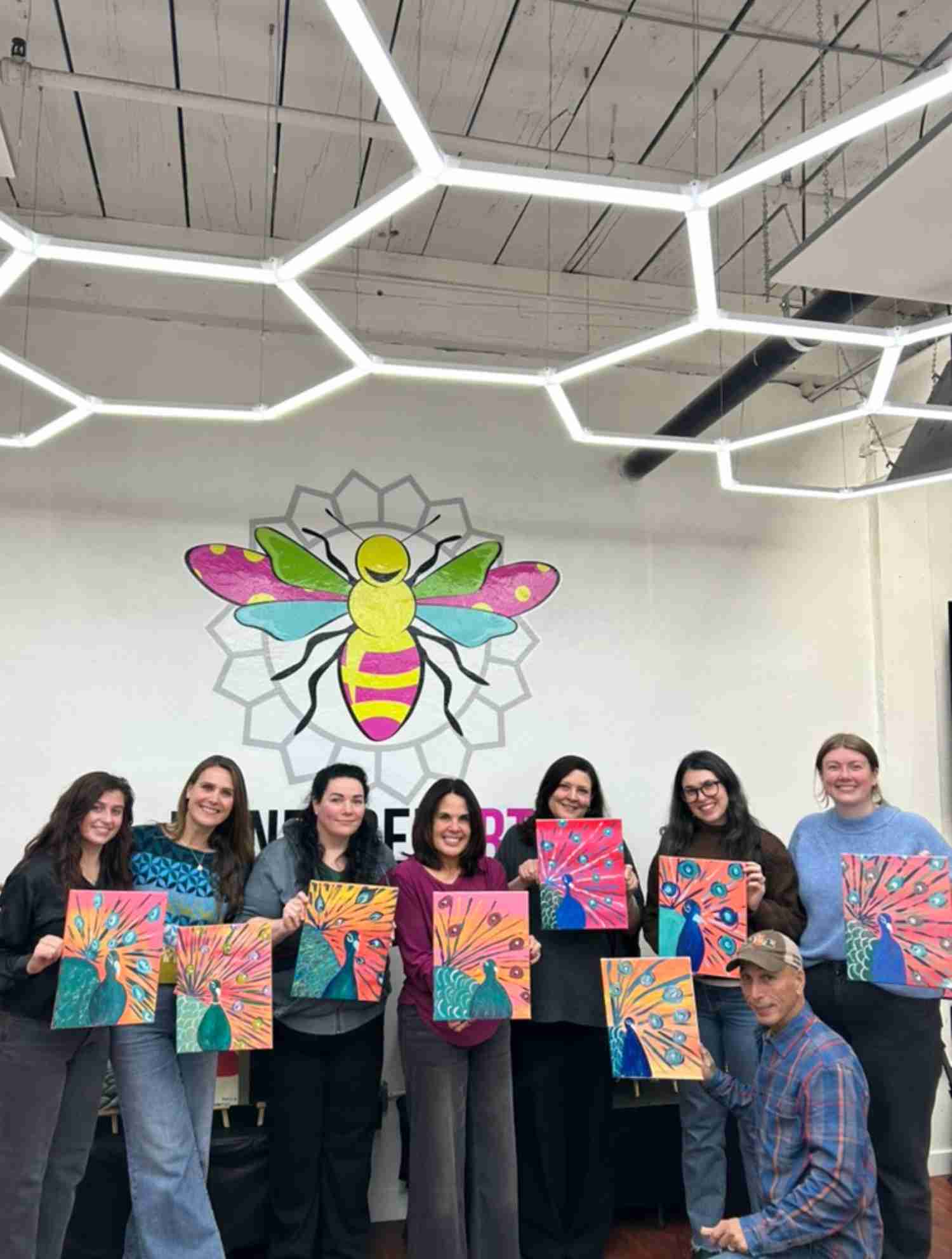 Zoom call gallery showing multiple people smiling and holding colorful butterfly paintings.