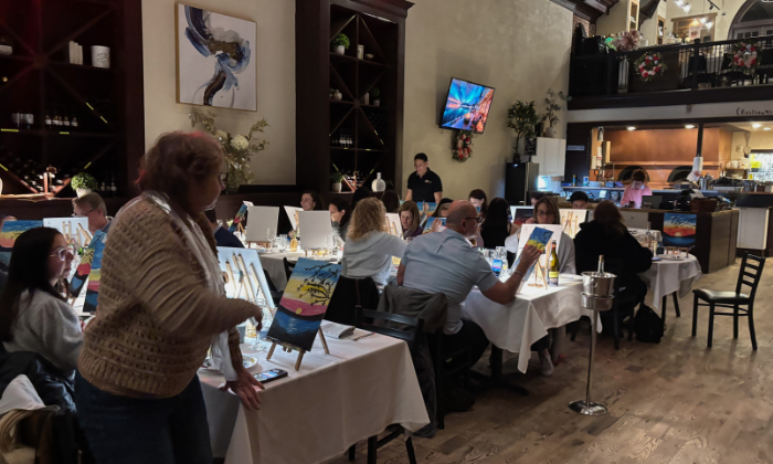 Group of people painting on canvases at a paint and sip event in a restaurant.