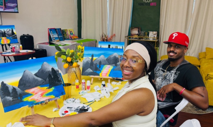 A couple sitting at a table with paintings of mountains and colorful rivers at a date night paint and sip.