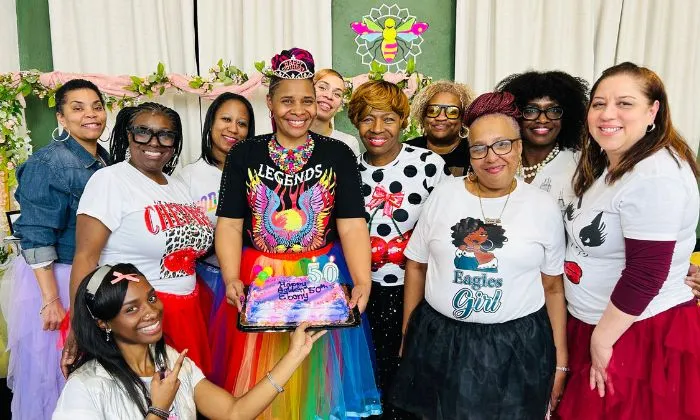 Smiling group of women celebrating with a colorful 50th birthday cake and festive outfits.