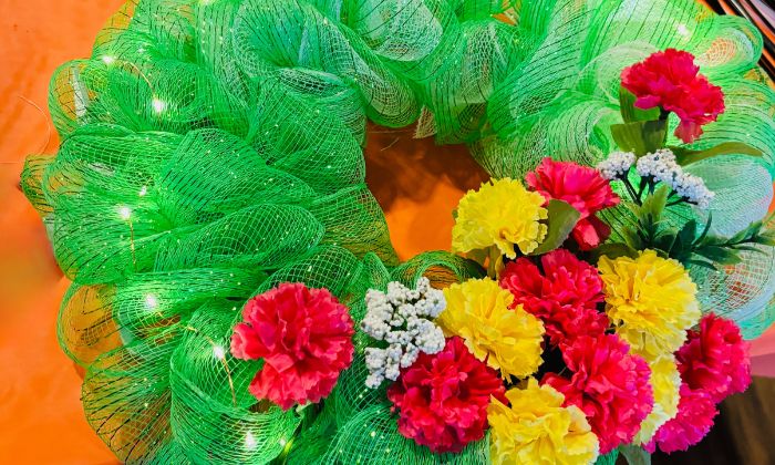 Decorative green wreath with yellow, red, and white artificial flowers and small lights.