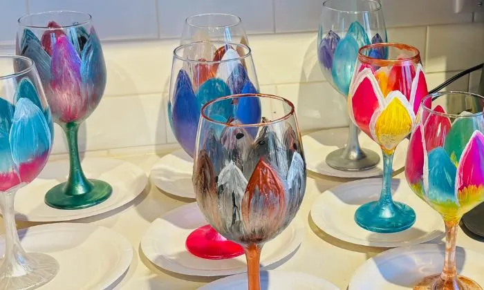 Assortment of colorful hand-painted wine glasses with floral designs on white paper plates.