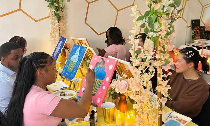 Group of people painting cupcake pictures on canvases at a decorated indoor paint and sip studio event.