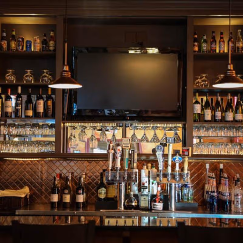 Bar counter with multiple beer taps, bottles of liquor, glasses, and a large TV mounted on the wall.