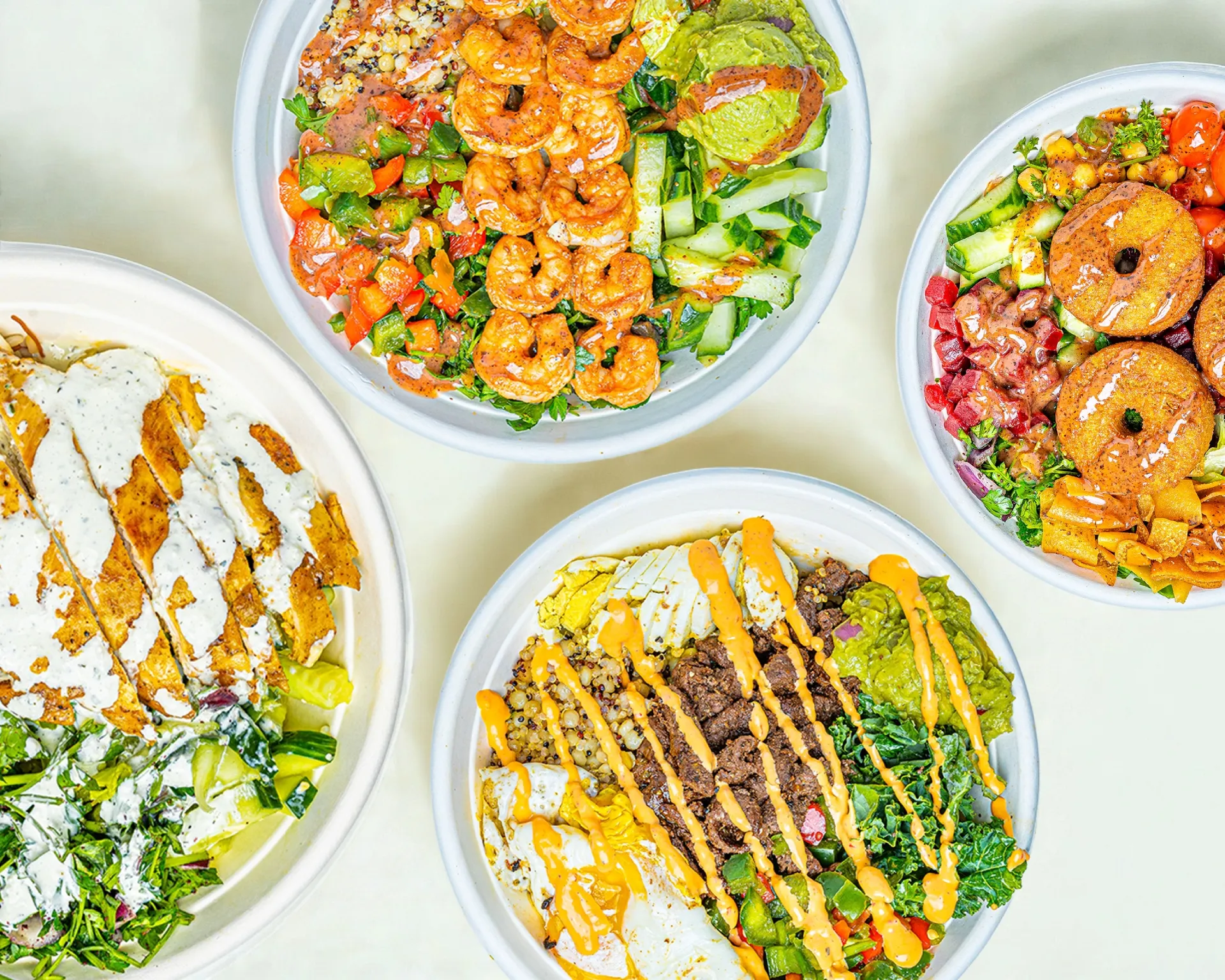 Overhead view of four Bowl Appetit bowls with shrimp, steak, chicken and falafel