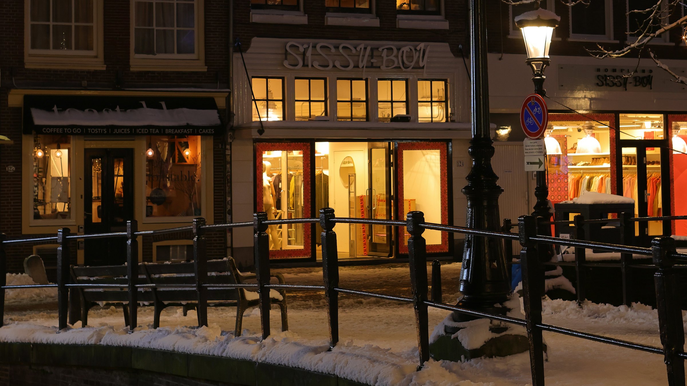 A snowy winter street with illuminated storefronts at night