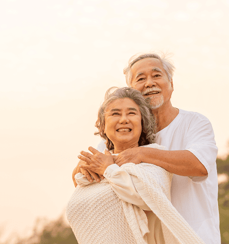 Smiling elderly couple embracing outdoors with a soft sunset background.