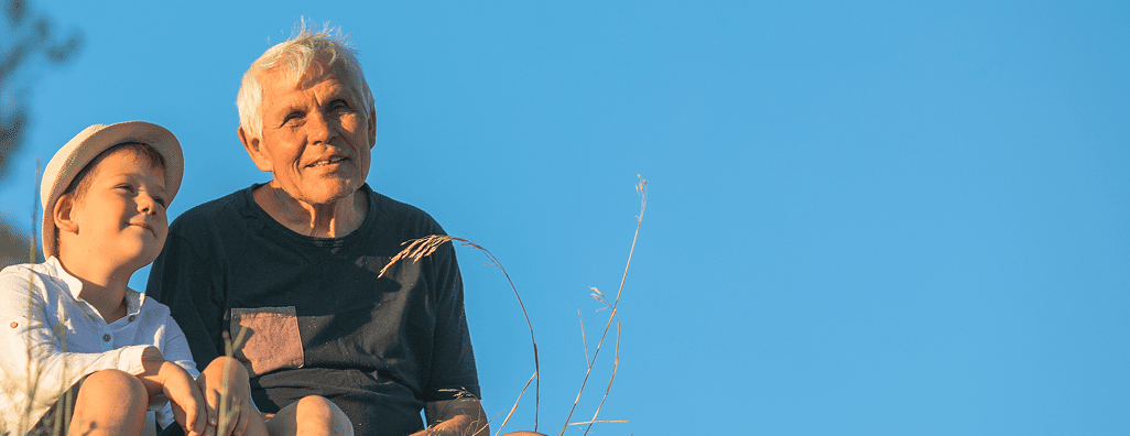 Older man on fixed income and good medicare coverage, and young boy sitting outdoors with a clear blue sky background.