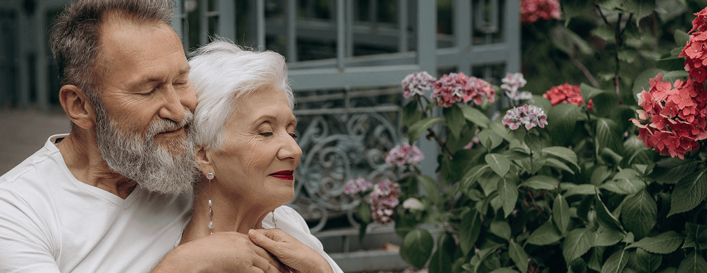 Senior couple embracing peacefully near blooming hydrangea flowers outdoors.
