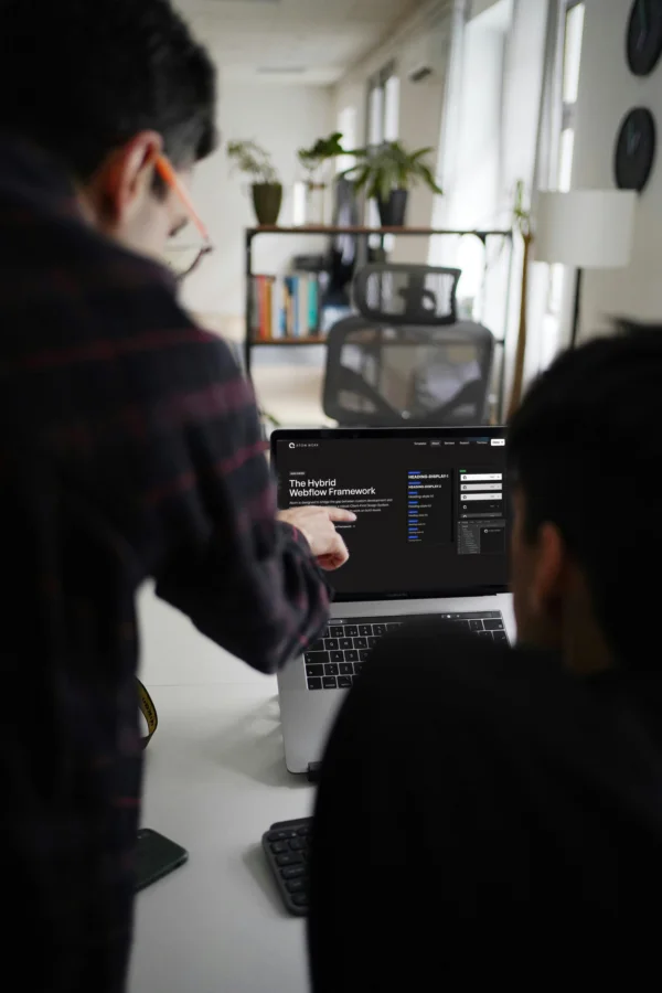 Two people looking at a laptop screen displaying 'The Hybrid Webflow Framework' in a modern office setting.
