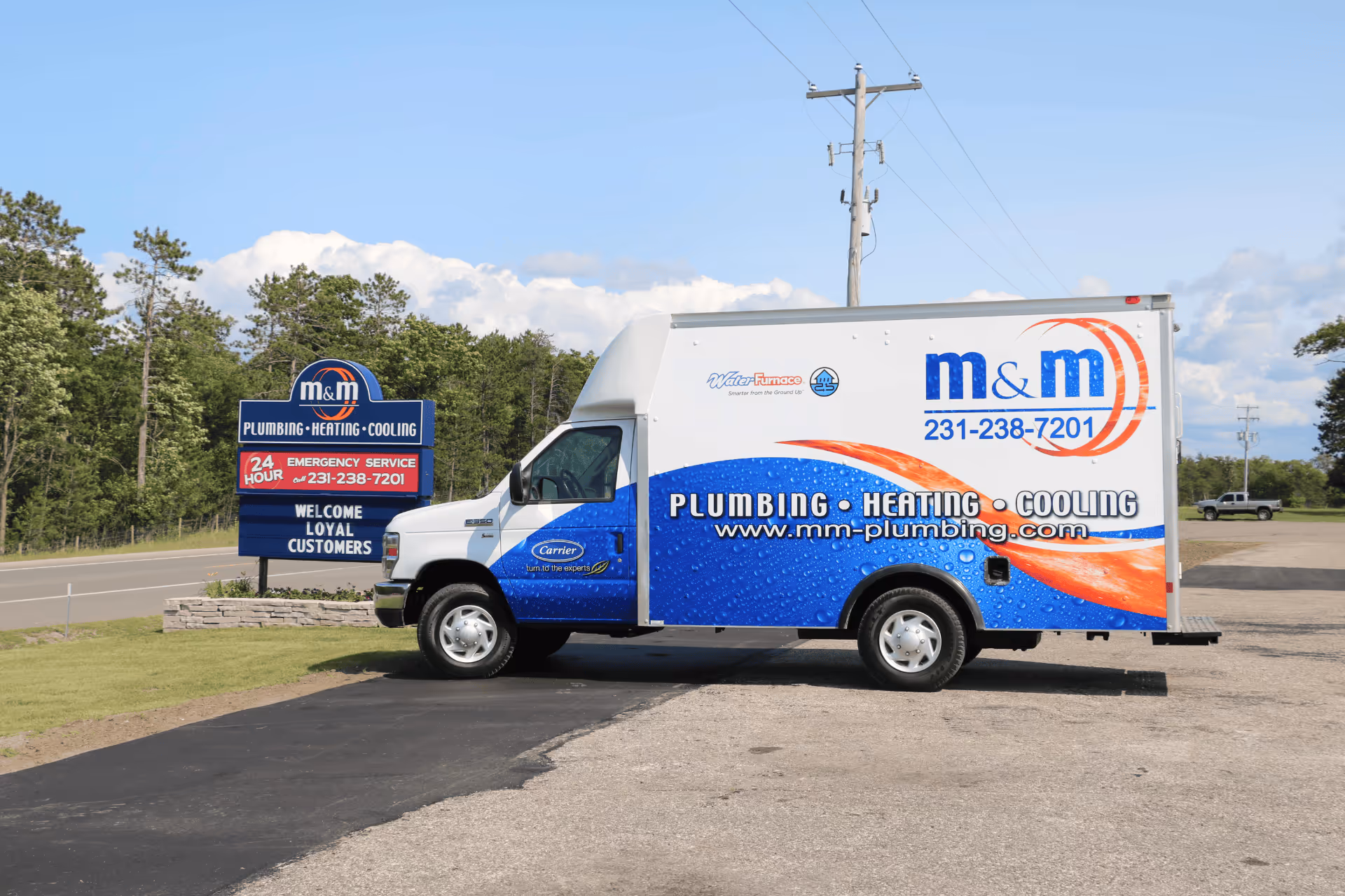 M&M Plumbing, Heating, and Cooling service truck parked next to company sign on a sunny day.