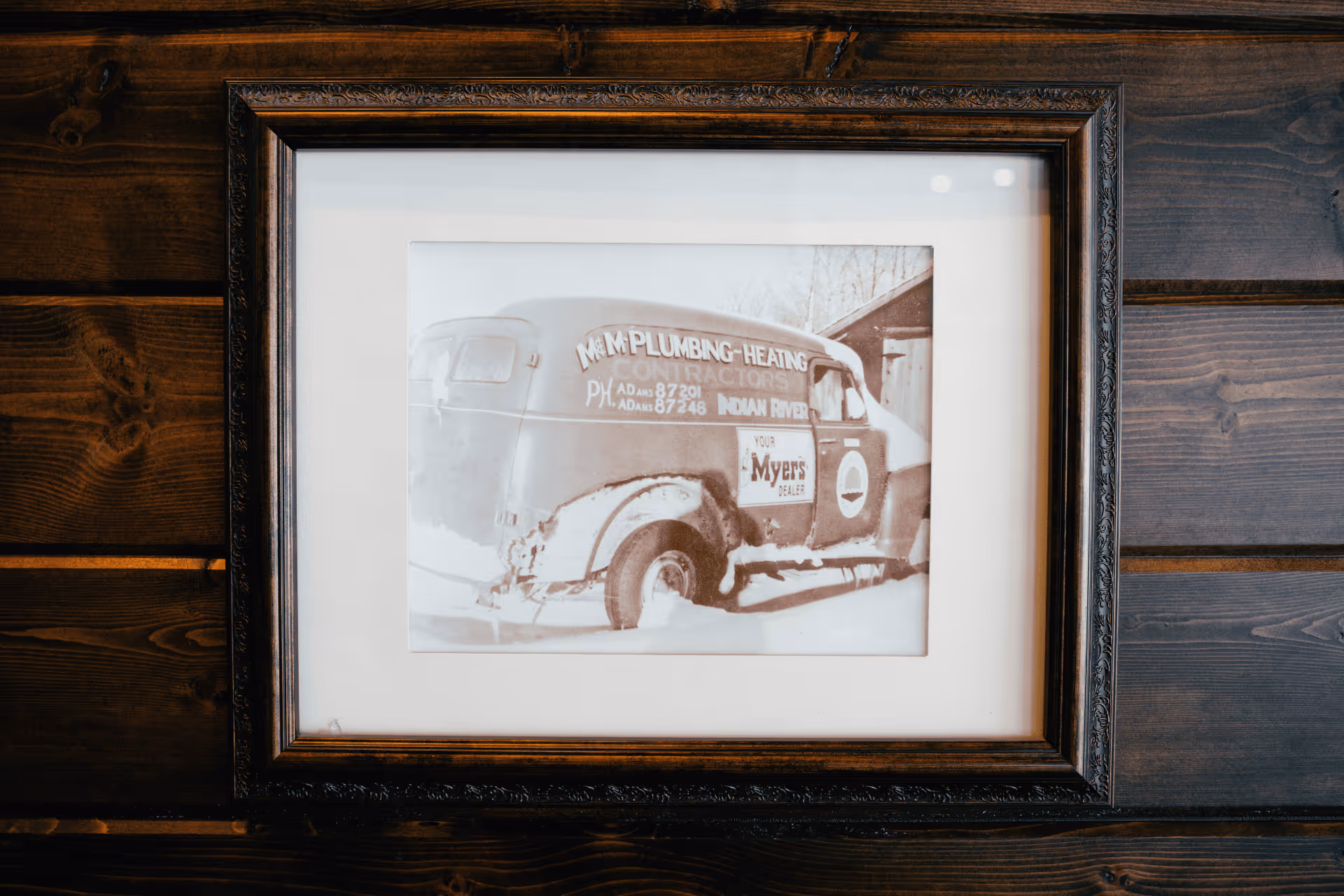 Framed black-and-white photo of an old M&M Plumbing-Heating service van covered in snow.
