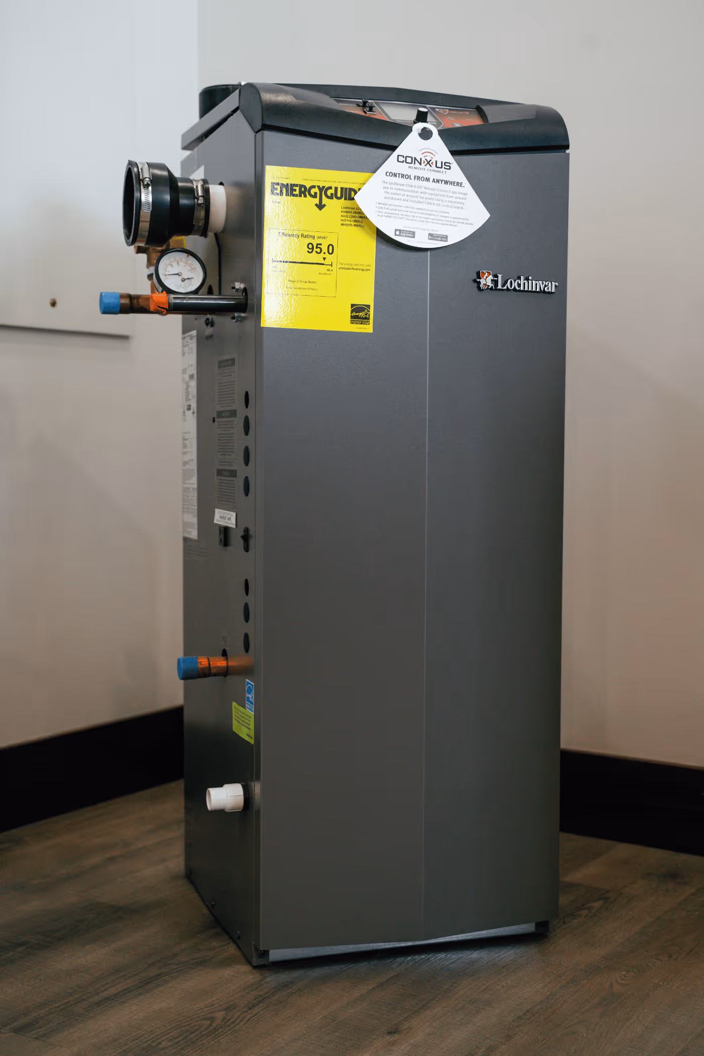 Lochinvar boiler or furnace unit with energy guide label and pressure gauge installed on a wooden floor.