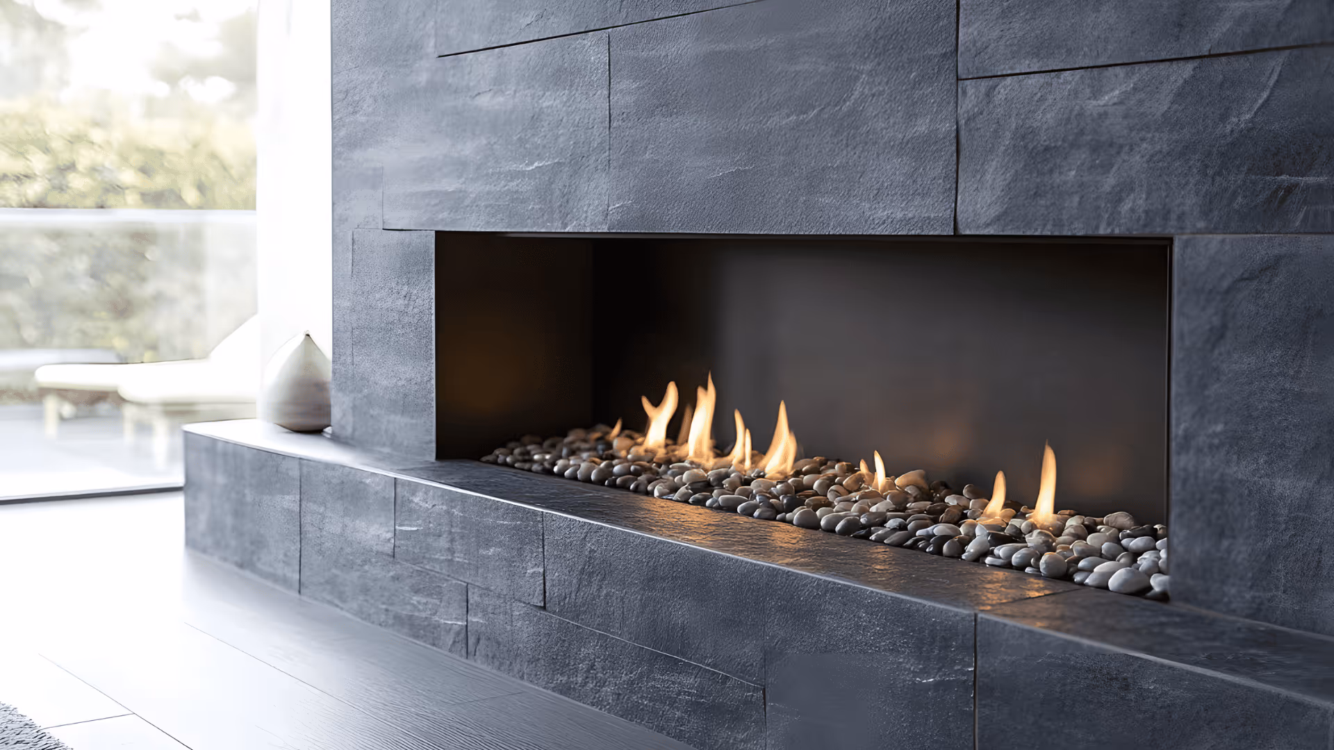 Modern gas fireplace with flames over decorative stones set in a sleek dark stone surround.