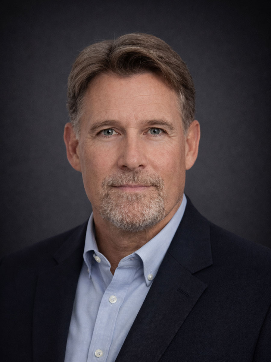 Middle-aged man with light brown hair, beard, and blue eyes wearing a navy suit and light blue shirt, facing forward.