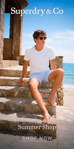 Young man in white shirt and shorts sitting on stone steps by the beach under blue sky.