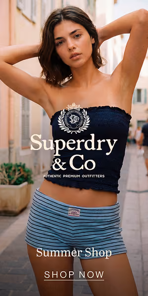 Woman with arms raised wearing a black tube top and striped shorts posing outdoors on a narrow street.