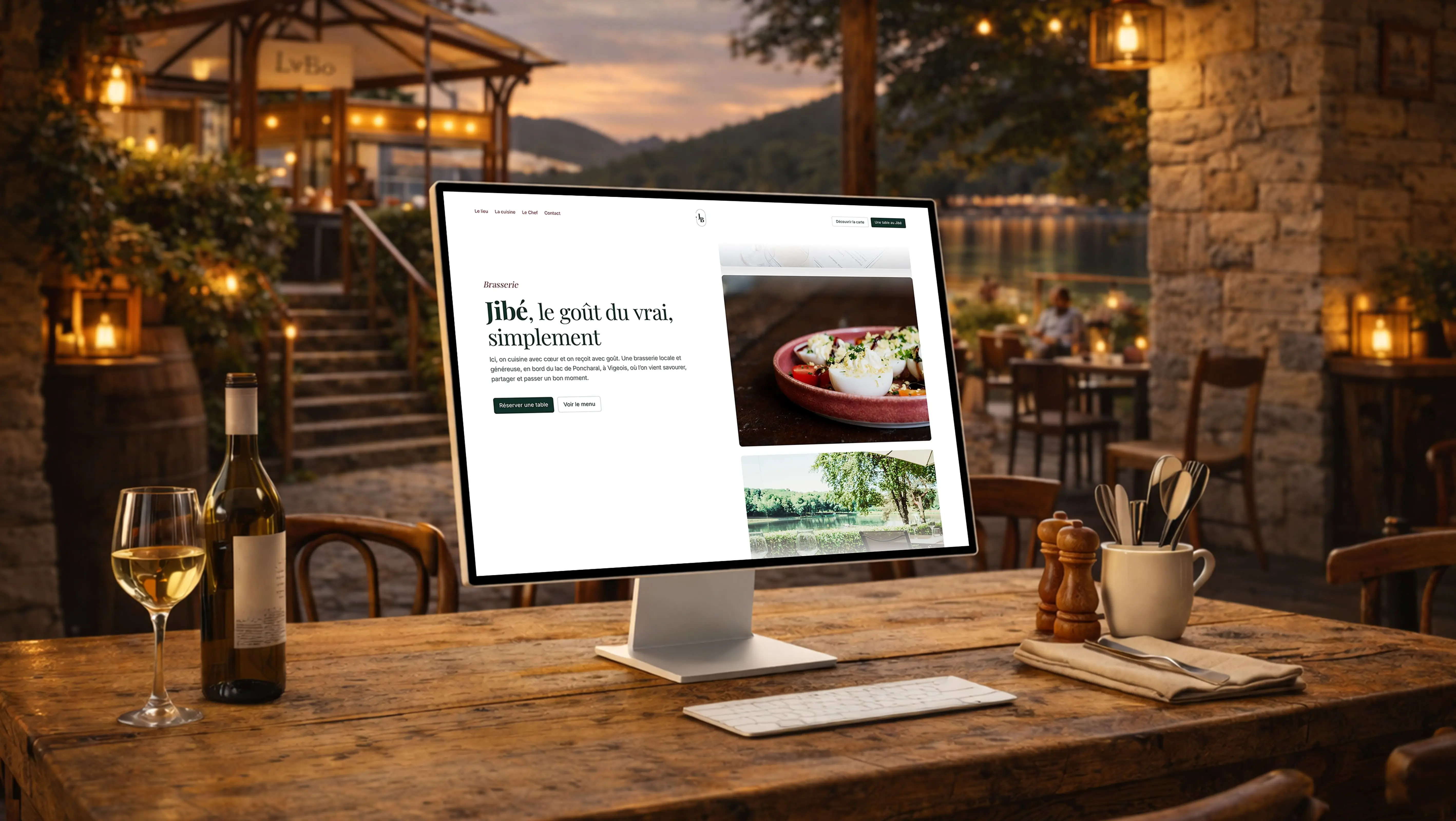 Mockup du site Jibé affiché sur un iMac posé sur une table en bois rustique, dans un restaurant au bord d'un lac