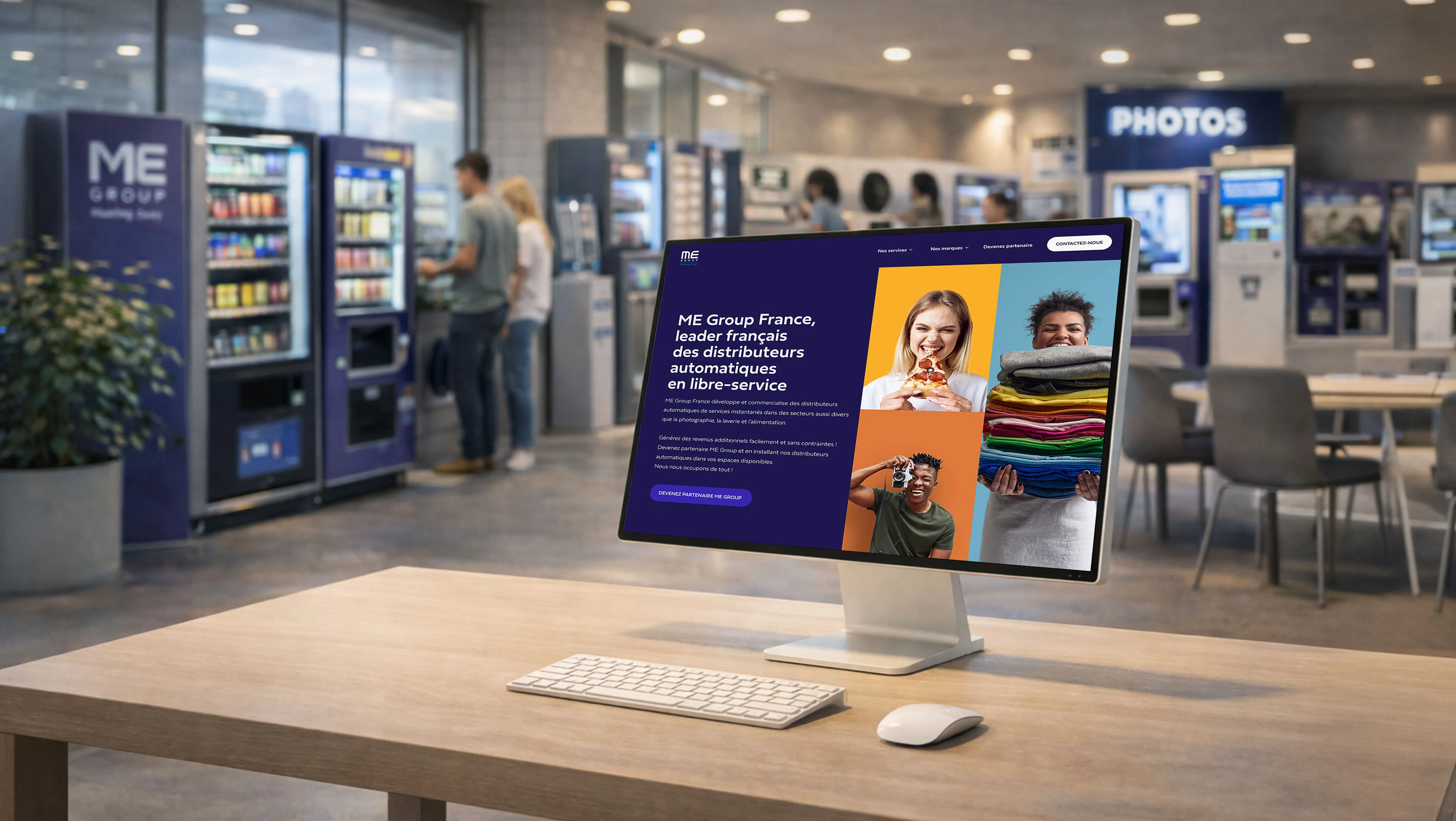 Mockup du site ME Group France affiché sur un iMac posé sur un comptoir, dans un espace de distributeurs automatiques en libre-service