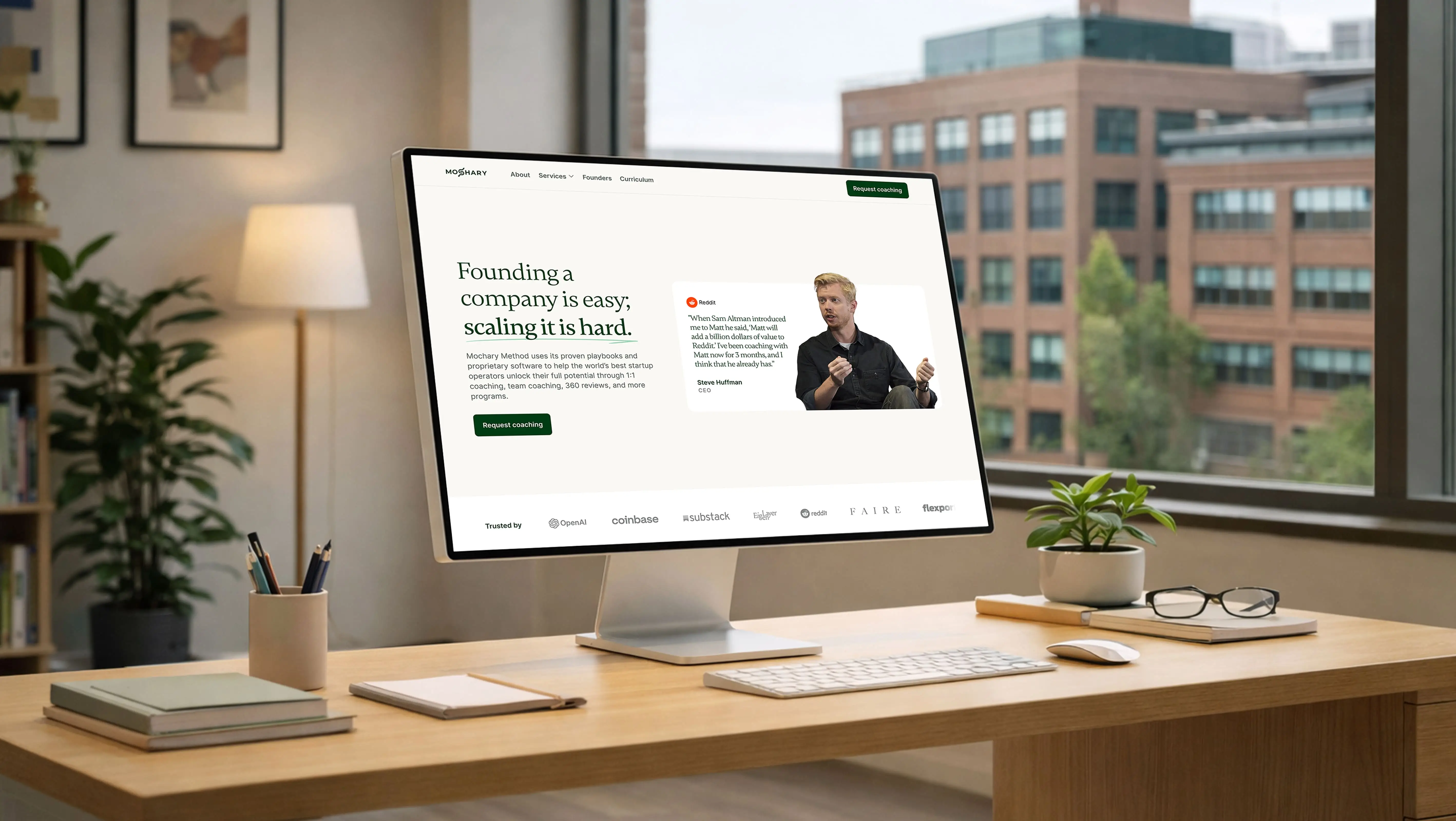 Mockup du site Mochary Method affiché sur un iMac dans un bureau lumineux aux tons naturels, avec une interface de coaching startup et des logos de clients comme OpenAI et Reddit visibles
