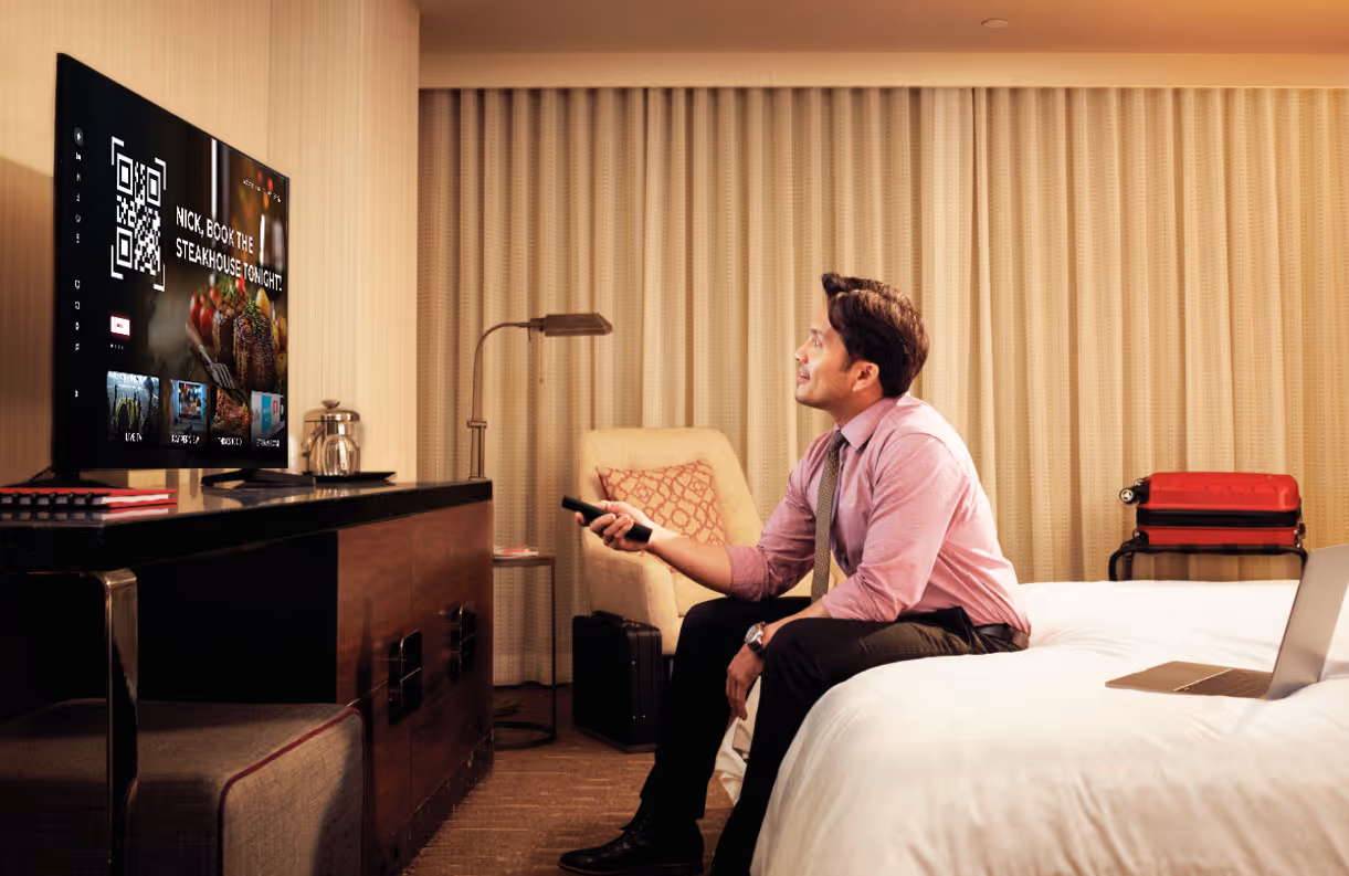 A man in a pink shirt is watching TV.